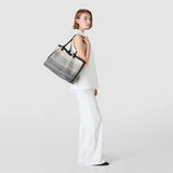 Side view: Model wearing SECRET TOTE BAG IN CANVAS casually over the shoulder; embroidered white-and-black dégradé canvas, black leather handles, roomy, paired with a white suit against a neutral background.