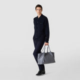 Frontal view: SECRET TOTE BAG IN CACHEMIRE LEATHER AND MOSAICO — grey Mosaico bag carried at the side, man in a dark outfit walking against a neutral background, visible embossed Mosaico strip.