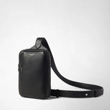 Frontal view: SLING BACKPACK IN CACHEMIRE LEATHER AND MOSAICO — black, fine-grain Cachemire leather sling backpack stands on a white background; adjustable shoulder strap with Mosaico detail lies to the side; front labeled 'SERAPIAN'.