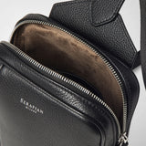 Detail view: SLING BACKPACK IN CACHEMIRE LEATHER AND MOSAICO — black pebbled leather sling with open zipper, brown interior lining visible, 'SERAPIAN MILANO' print.