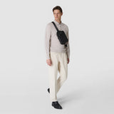 Frontal view: SLING BACKPACK IN CACHEMIRE LEATHER AND MOSAICO, black sling backpack worn across the chest by a male model against a light studio background.