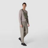 Frontal view: SLING BACKPACK IN CACHEMIRE LEATHER AND MOSAICO worn by a man across his chest, showing green cachemire leather and Mosaico detail, neutral studio background.