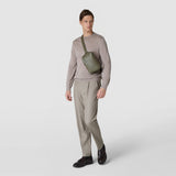 Frontal view: A man wears the SLING BACKPACK IN CACHEMIRE LEATHER AND MOSAICO across his chest; an olive-green, rectangular textured leather bag with a Mosaico strap against a light background; 'SERAPIAN' on the front.