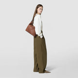 Side view of a woman casually carrying the ANI SHOULDER BAG IN CACHEMIRE LEATHER AND MOSAICO in tobacco brown over her shoulder. The bag appears elegant and understated.