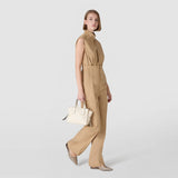 Side view — woman in profile walking, carrying SMALL MARO BAG IN CACHEMIRE LEATHER AND MOSAICO in Cream by hand; Mosaico weave at top, knotted nappa leather strips, light neutral background.