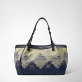 Frontal view: SMALL SECRET TOTE BAG IN DENIM AND RAFFIA shows an upright navy blue jacquard denim tote with a raffia-woven geometric pattern, two shoulder straps, and gold 'SERAPIAN MILANO' lettering against a neutral background.