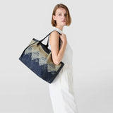 Side view: Model wearing SECRET TOTE BAG IN DENIM AND RAFFIA casually slung over her shoulder; navy-blue jacquard denim with raffia texture and geometric Mosaico pattern, light studio background.