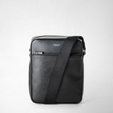 Front view: NORTH SOUTH CROSSBODY BAG IN EVOLUZIONE LEATHER, shows the black flat front with an external zip pocket and a strap draped diagonally against a light background; visible 'SERAPIAN MILANO' lettering.