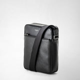 Frontal view: NORTH SOUTH CROSSBODY BAG IN EVOLUZIONE LEATHER lies on a neutral background, showing textured black calfskin leather, an adjustable shoulder strap at the front, and the 'SERAPIAN MILANO' logo.