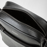 Detail view: NORTH SOUTH CROSSBODY BAG IN EVOLUZIONE LEATHER shows an open main compartment with an open zipper, a front zip pocket in textured black leather; 'SERAPIAN MILANO' logo.