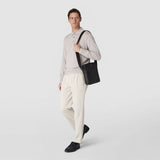 Frontal view: A model wears the NORTH SOUTH CROSSBODY BAG IN EVOLUZIONE LEATHER across the shoulder; flat black leather bag with adjustable strap against a light, neutral background.