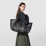 Side view of a woman wearing the MAXI SECRET TOTE BAG IN MOSAICO MESTIERI D'ARTE on her shoulder, large black bag with mosaic pattern.