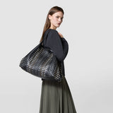 Side view of a woman carrying the MAXI SECRET TOTE BAG IN MOSAICO MESTIERI D'ARTE with black patterned leather and adjustable handles over her shoulder.