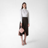 Frontal view: PETRA HANDBAG IN MOSAICO is held by a woman wearing a white blouse and dark skirt, showing its blush pink woven leather and tassel detail.