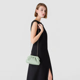 Side view: MINI SECRET CLUTCH BAG IN RIBBON MOSAICO, in Aqua, worn as a crossbody bag by a woman in a black dress; visible Ribbon-Mosaico with delicate chain strap.
