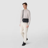 Frontal view: CAMERA CROSSBODY BAG IN STEPAN, worn crossbody over the shoulder on a standing model, black textured canvas with leather bands and adjustable strap.